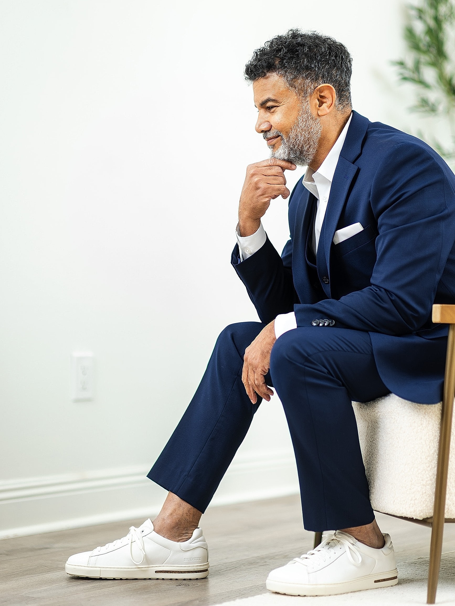 Man in navy suit sitting thoughtfully with sneakers.