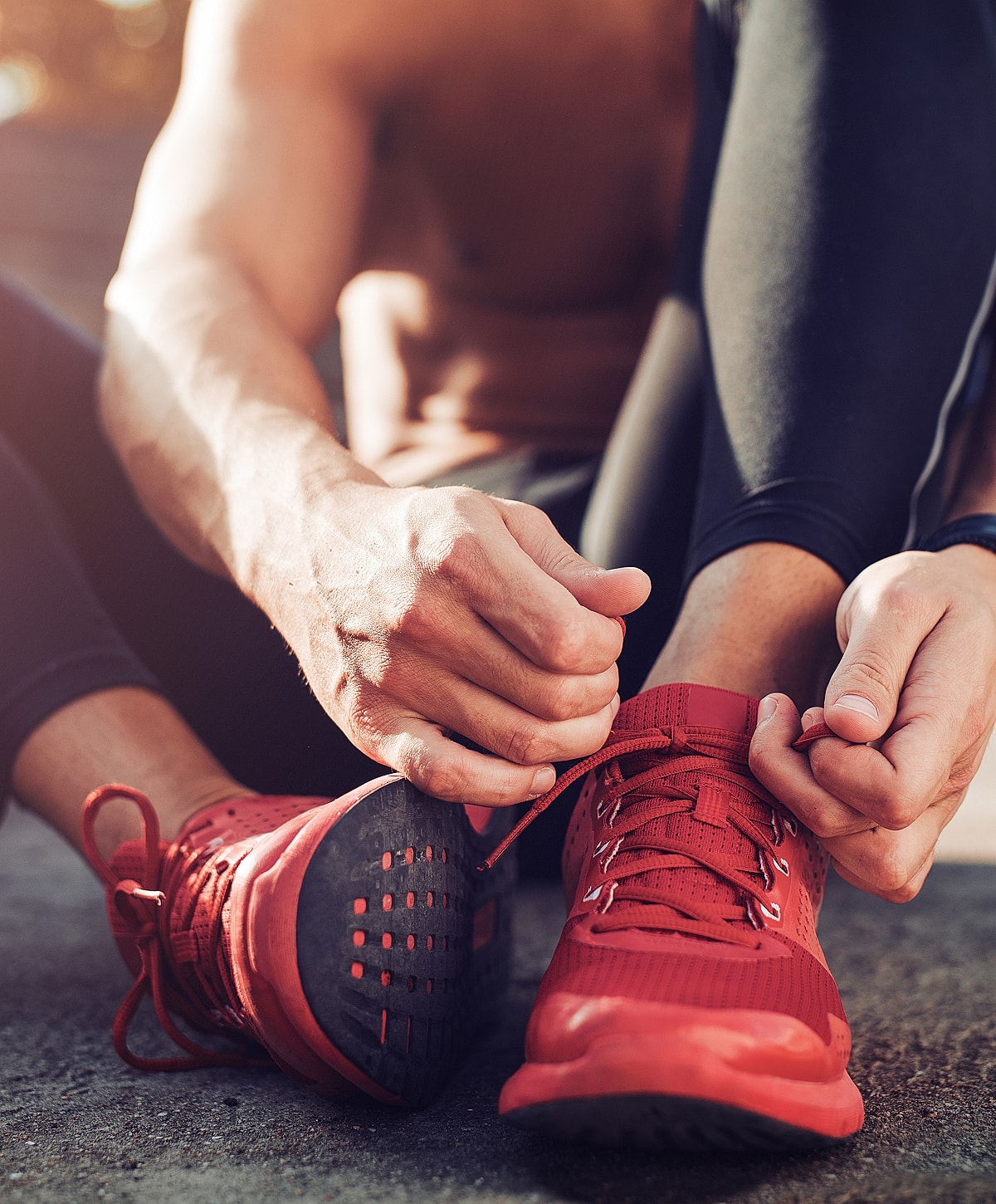 Person tying red athletic shoes outdoors.