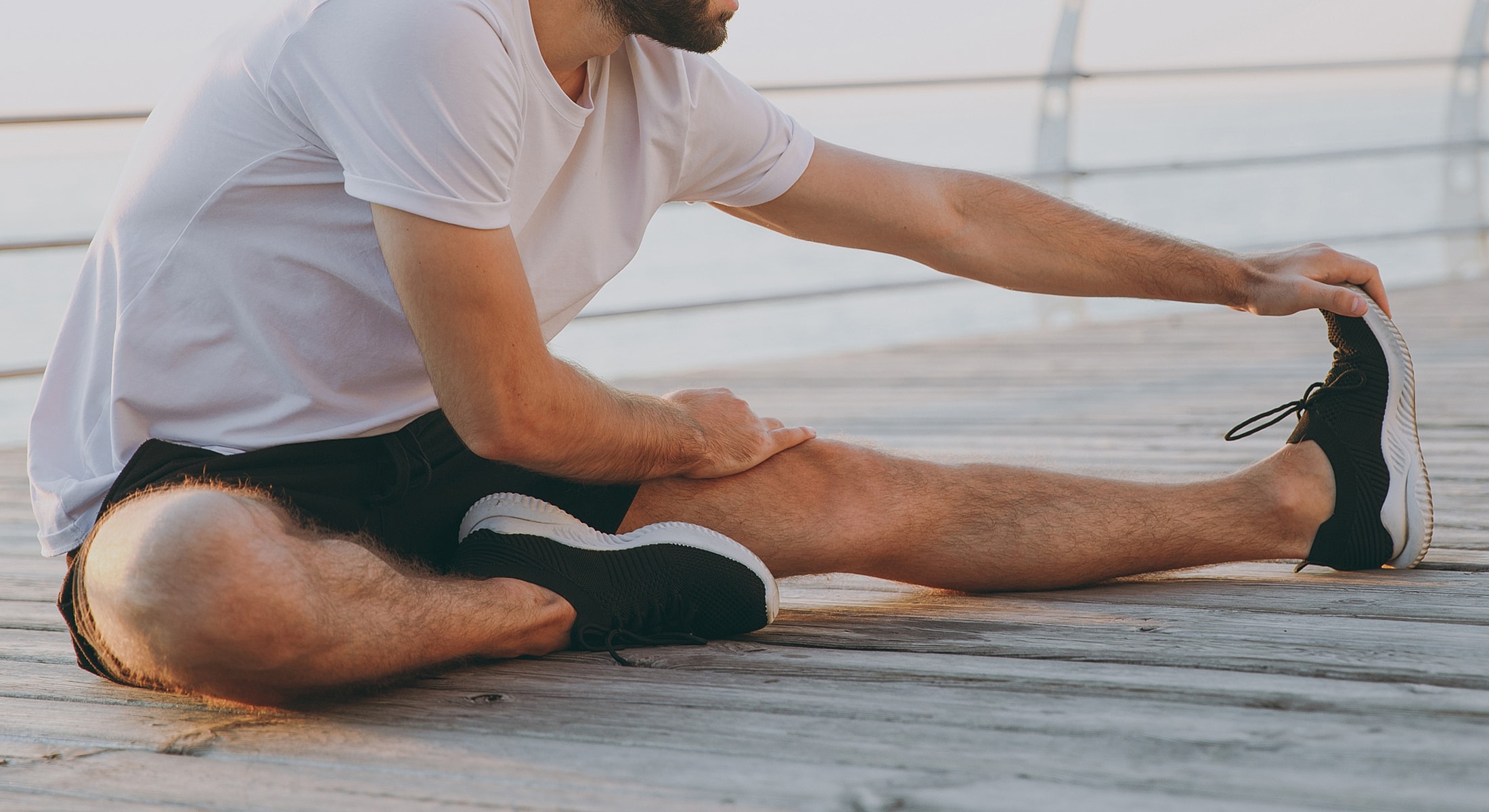 Man stretching on wooden pier at sunrise.