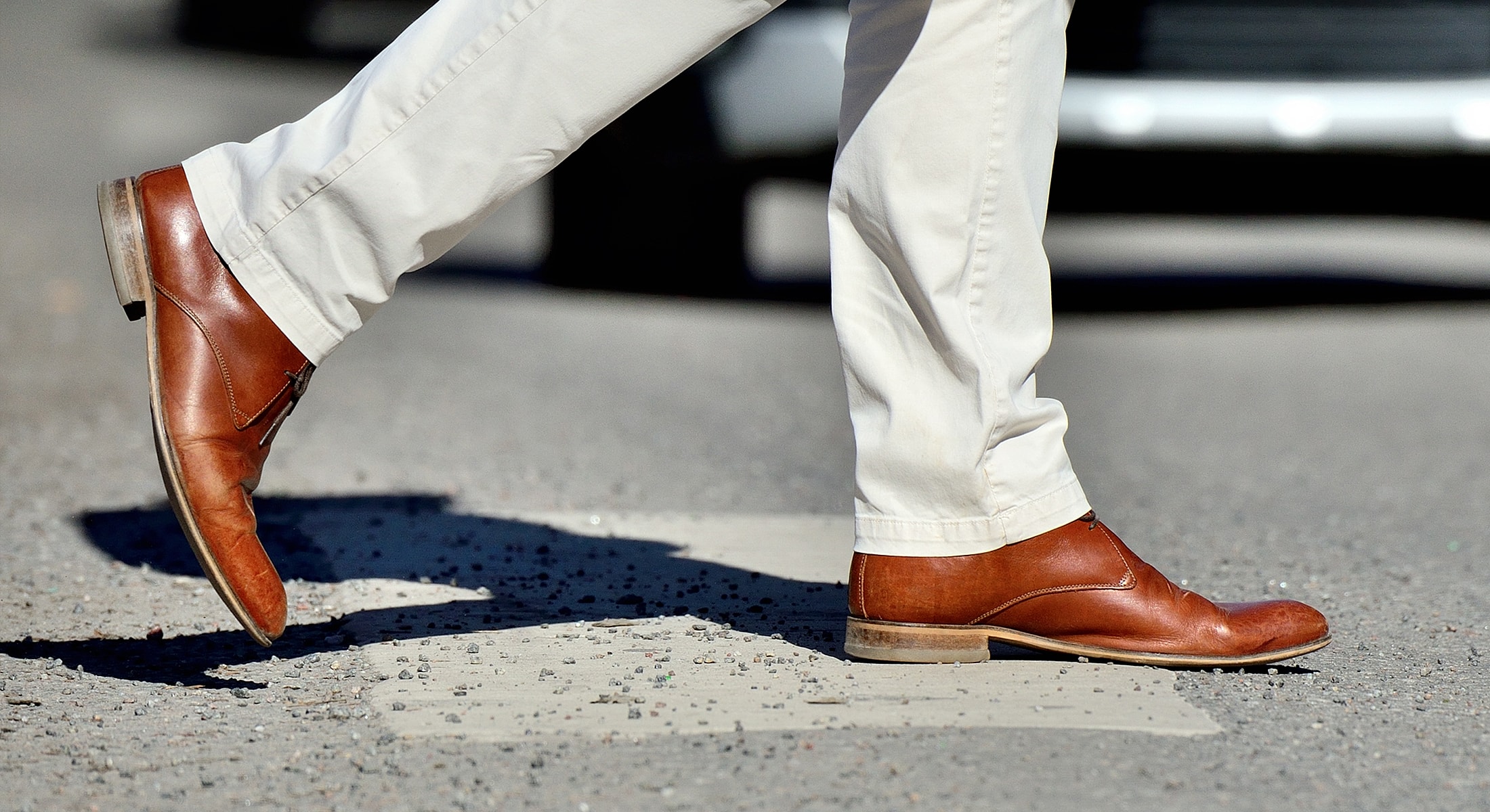 Brown leather shoes stepping on a crosswalk.