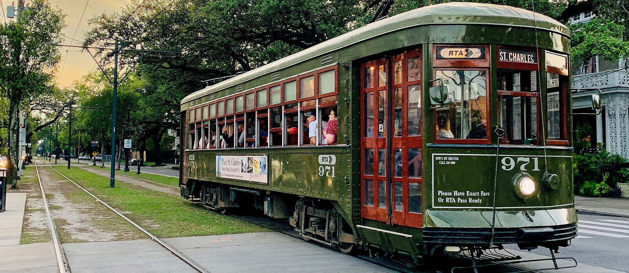 Historic streetcar traveling along green tree-lined street.