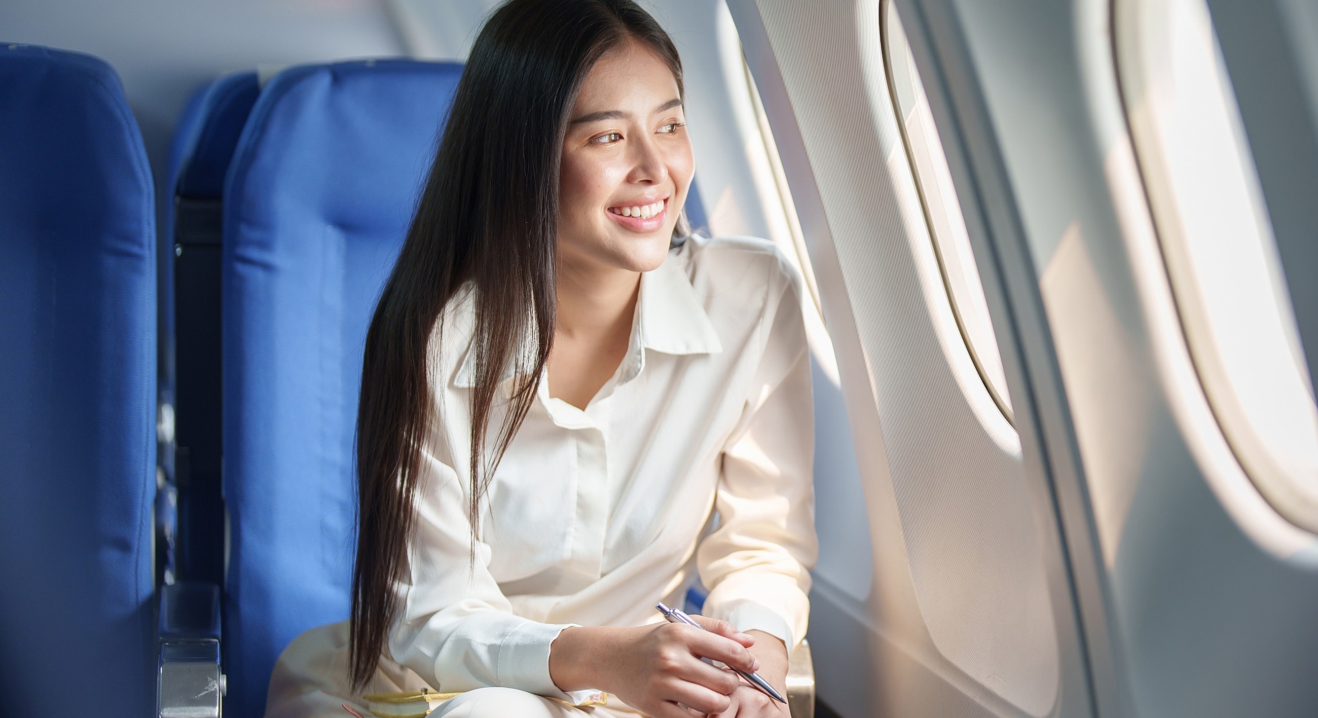 Woman looking out airplane window, smiling warmly.