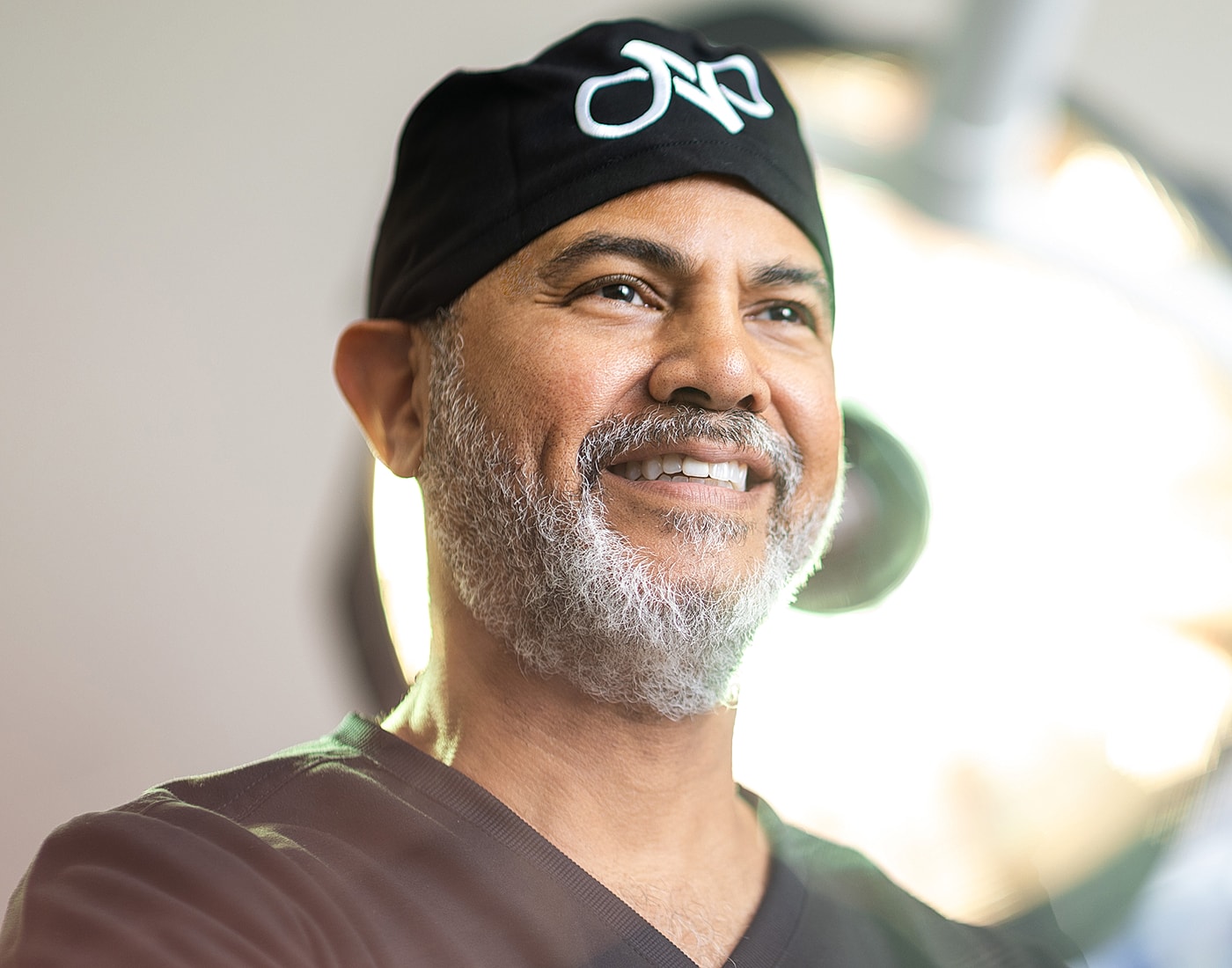 Smiling surgeon in medical attire with surgical lighting.
